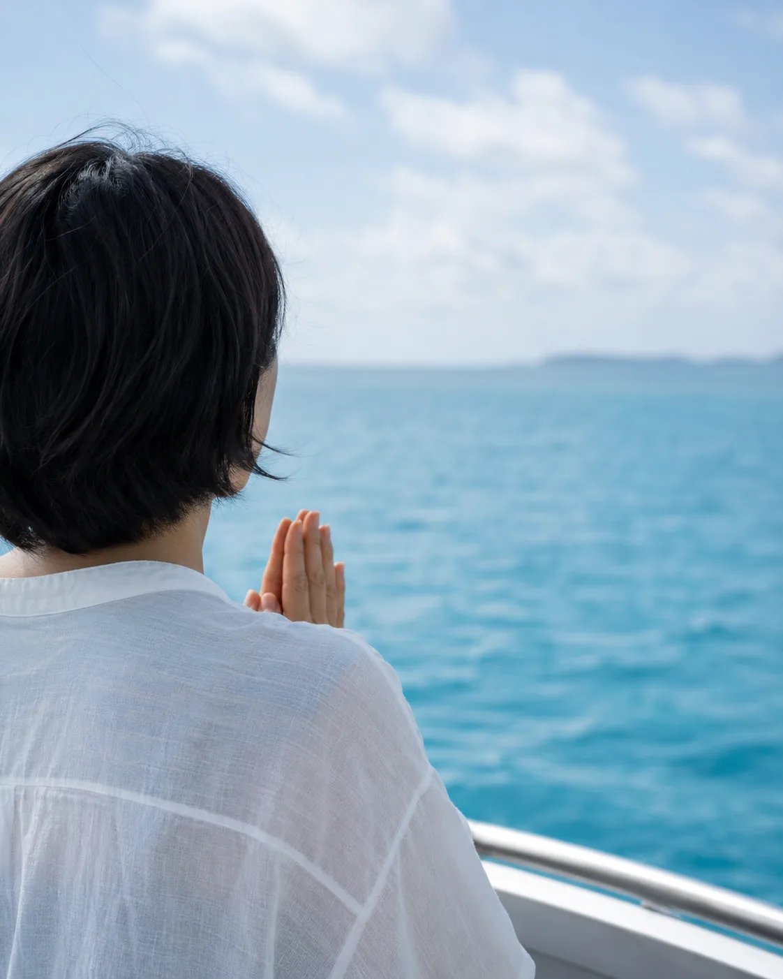 船上から海に向かって手を合わせる人